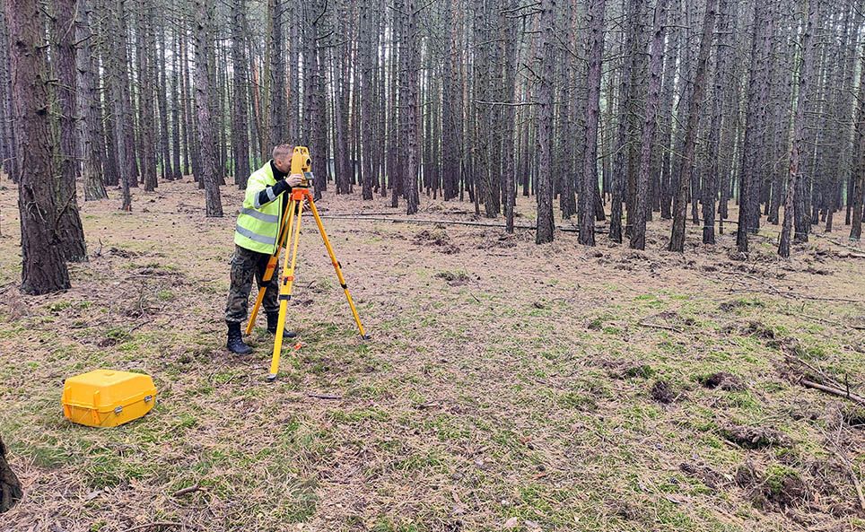Pracownik firmy geodezyjnej Explosive wykonuje usługę geodezyjną w lesie